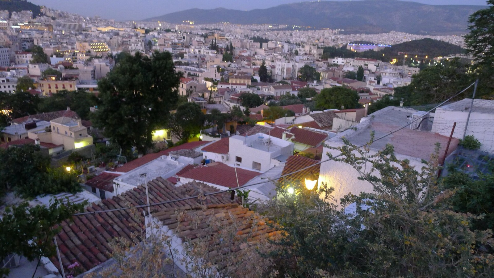 Tiled rooftops of Anafiotika at dusk with the lights of Athens beyond